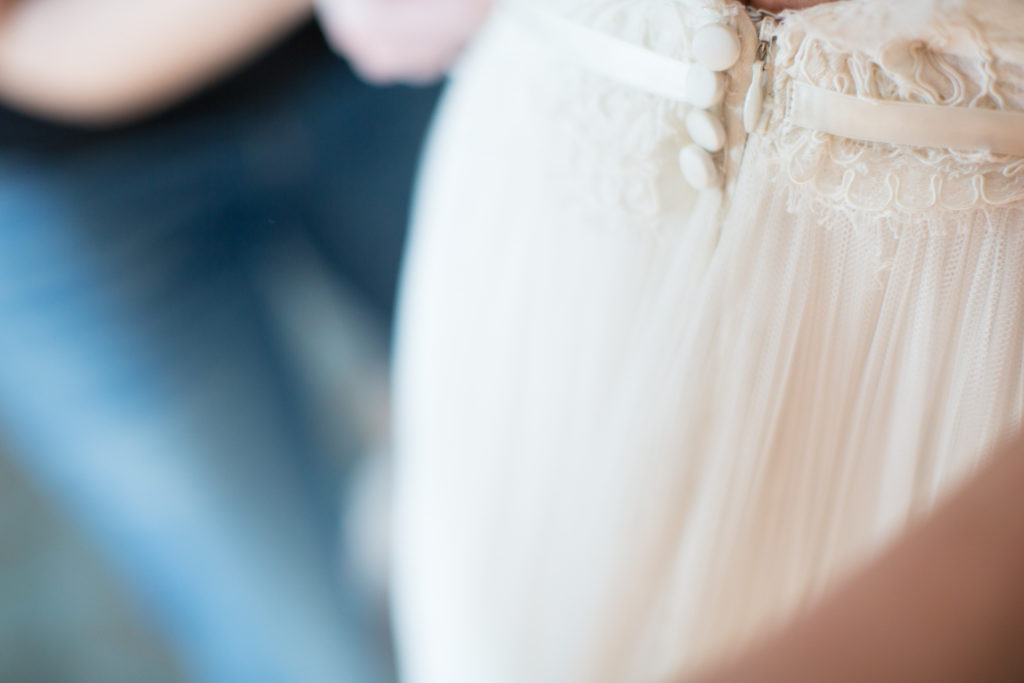 bride getting ready for wedding day. beautiful white wedding gown being buttoned.